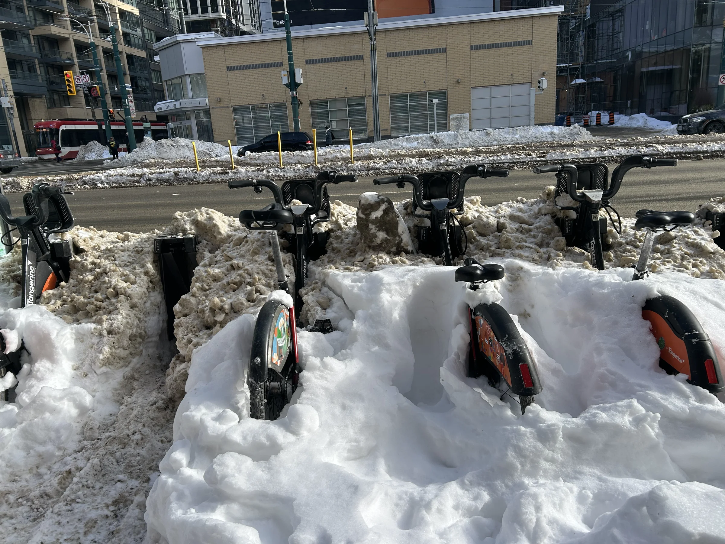Toronto bike-share bicycles buried in snow beside a streetcar route.